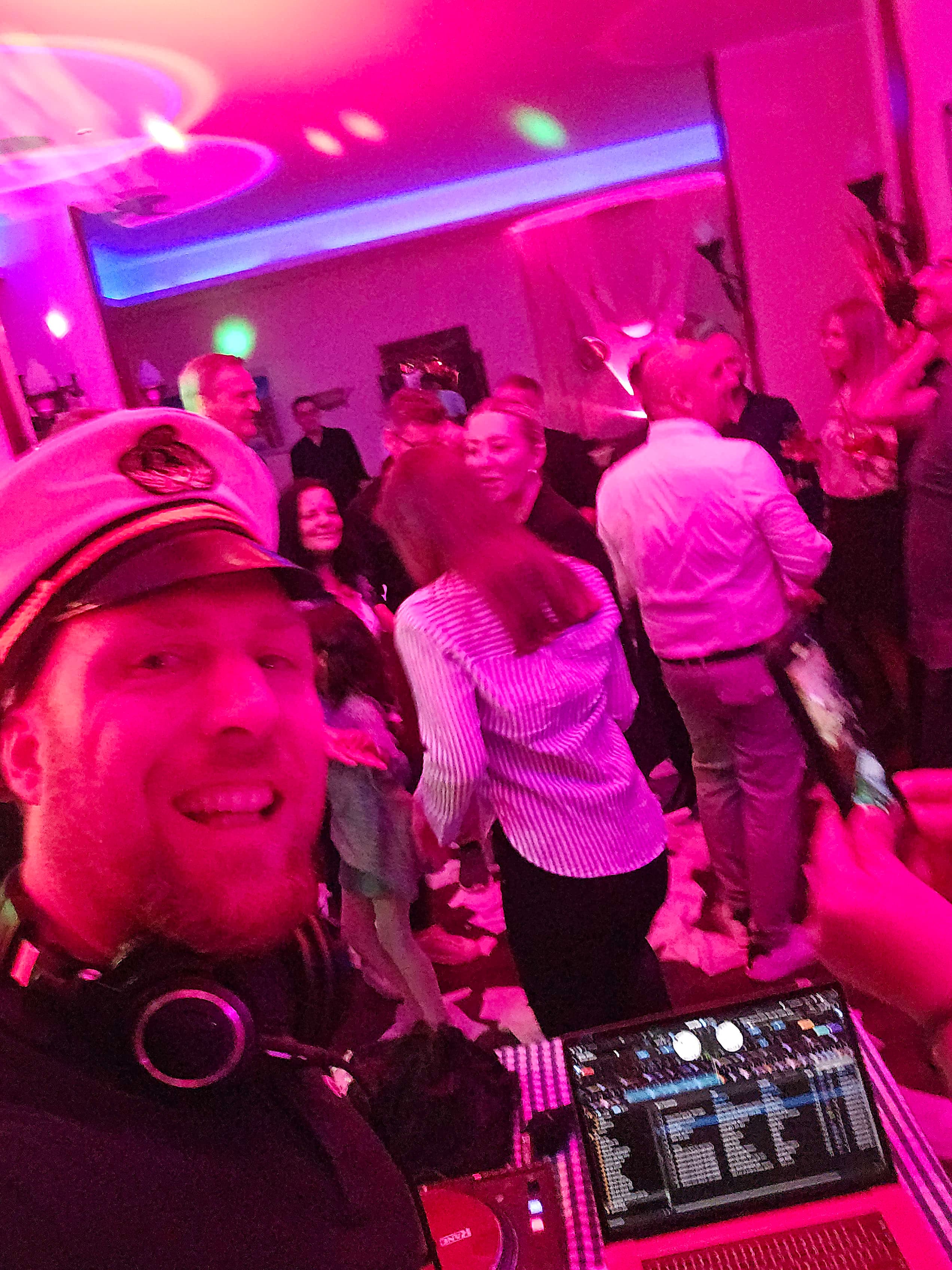 Tanzende Gäste vor dem DJ-Pult, beleuchtet von violetten und blauen LED-Lichtern – Platzhalterbild